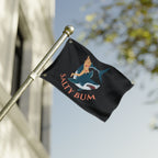 Flag with a shark and bikini-clad figure design, featuring the text 'Salty Bum', waving on a flagpole against a blurred background.
