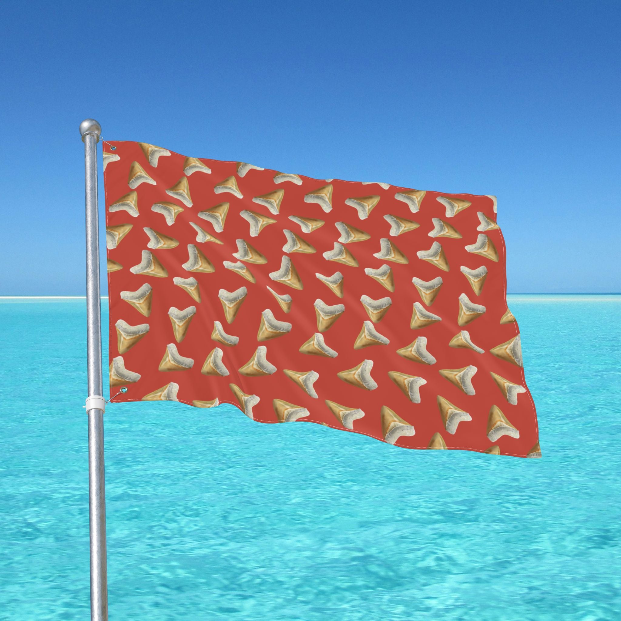 Red flag with shark tooth pattern waving in the wind against a clear blue sky and ocean.