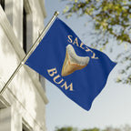 Flag with 'Salty Bum' text and a graphic of a corn dog against a blue background, waving in front of a building.