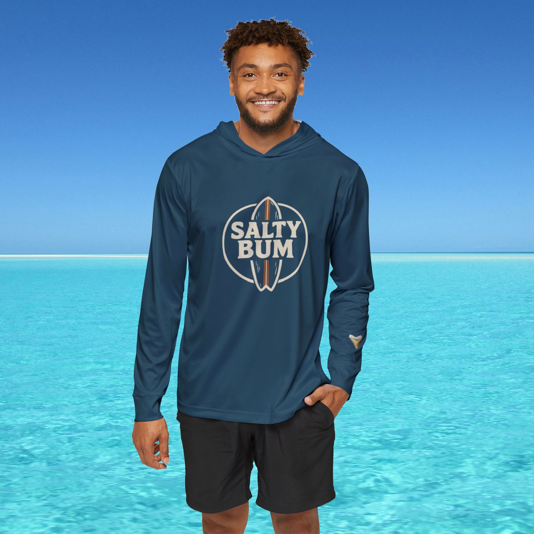 Man wearing a blue hoodie with 'Salty Bum' logo in front of clear blue water and sky.