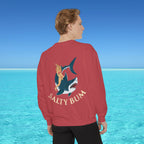 Person wearing a red sweatshirt with a shark and bikini design, standing in front of a blue ocean.