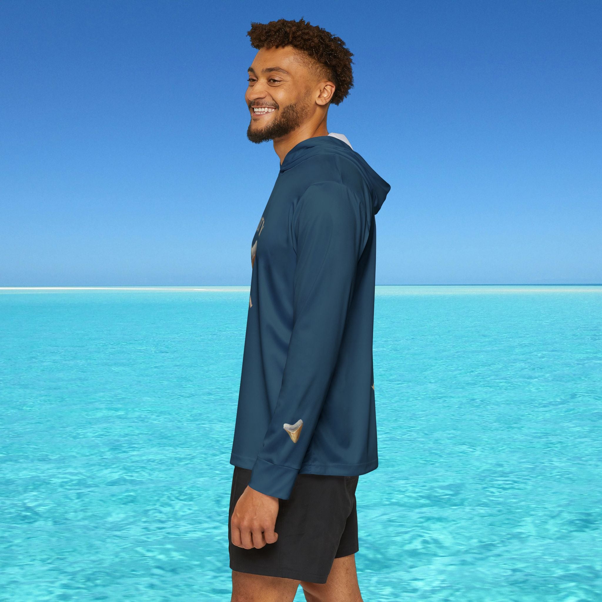 Man wearing a blue jacket standing on a beach with clear blue water and sky.