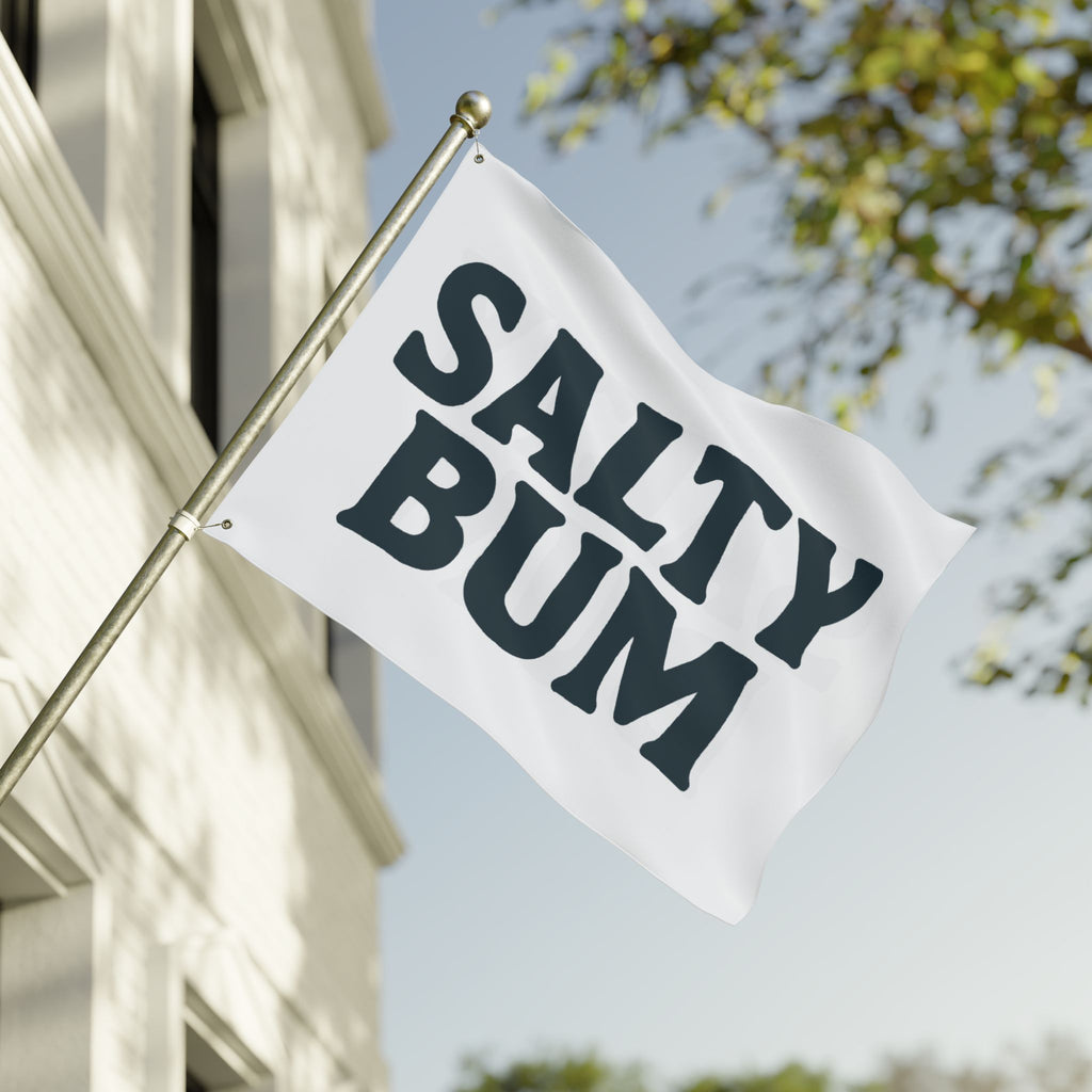 Flag with 'Salty Bum' text waving in front of a building and tree.