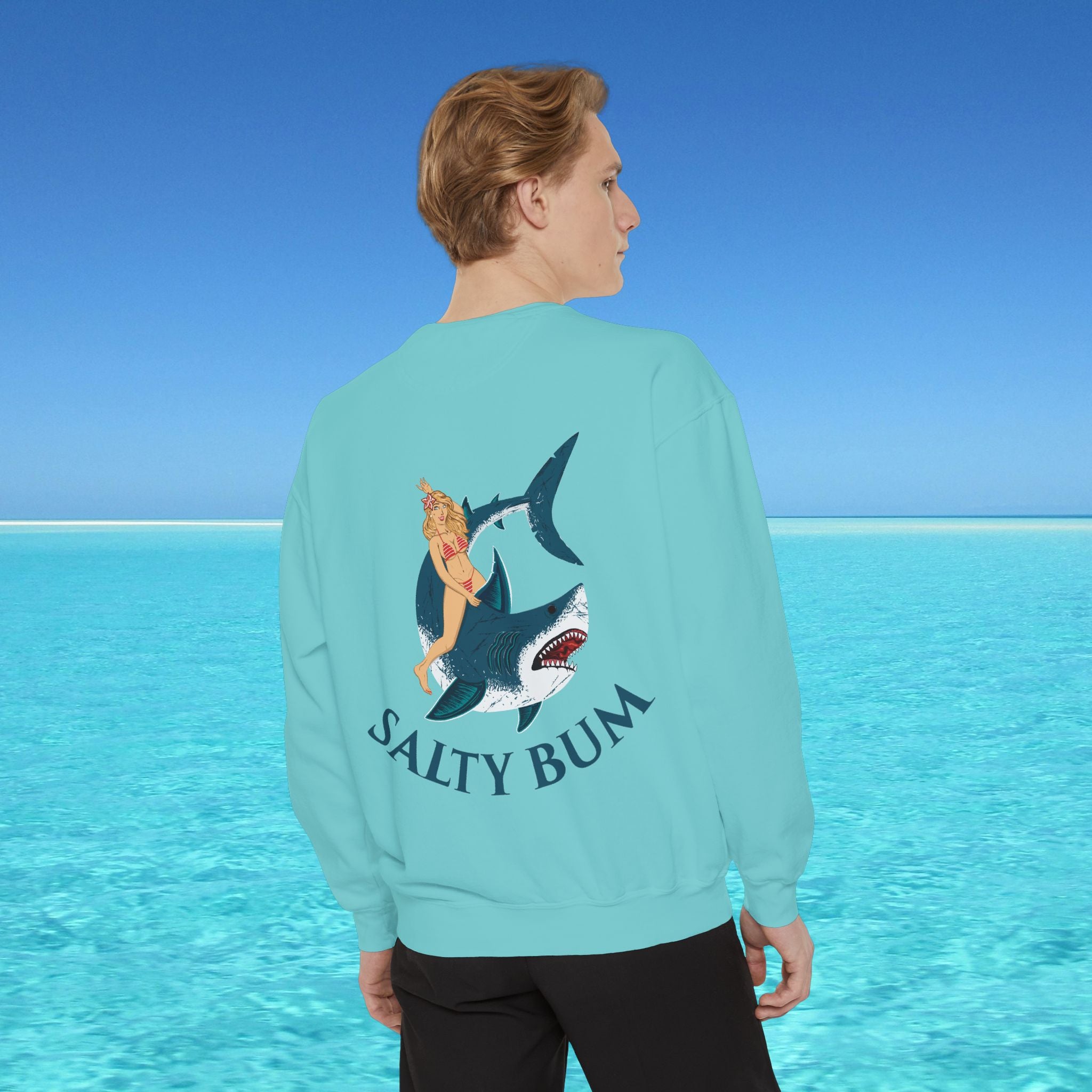 Person wearing a light blue sweatshirt with a shark and bikini graphic and 'Salty Bum' text, standing against a clear blue ocean background.