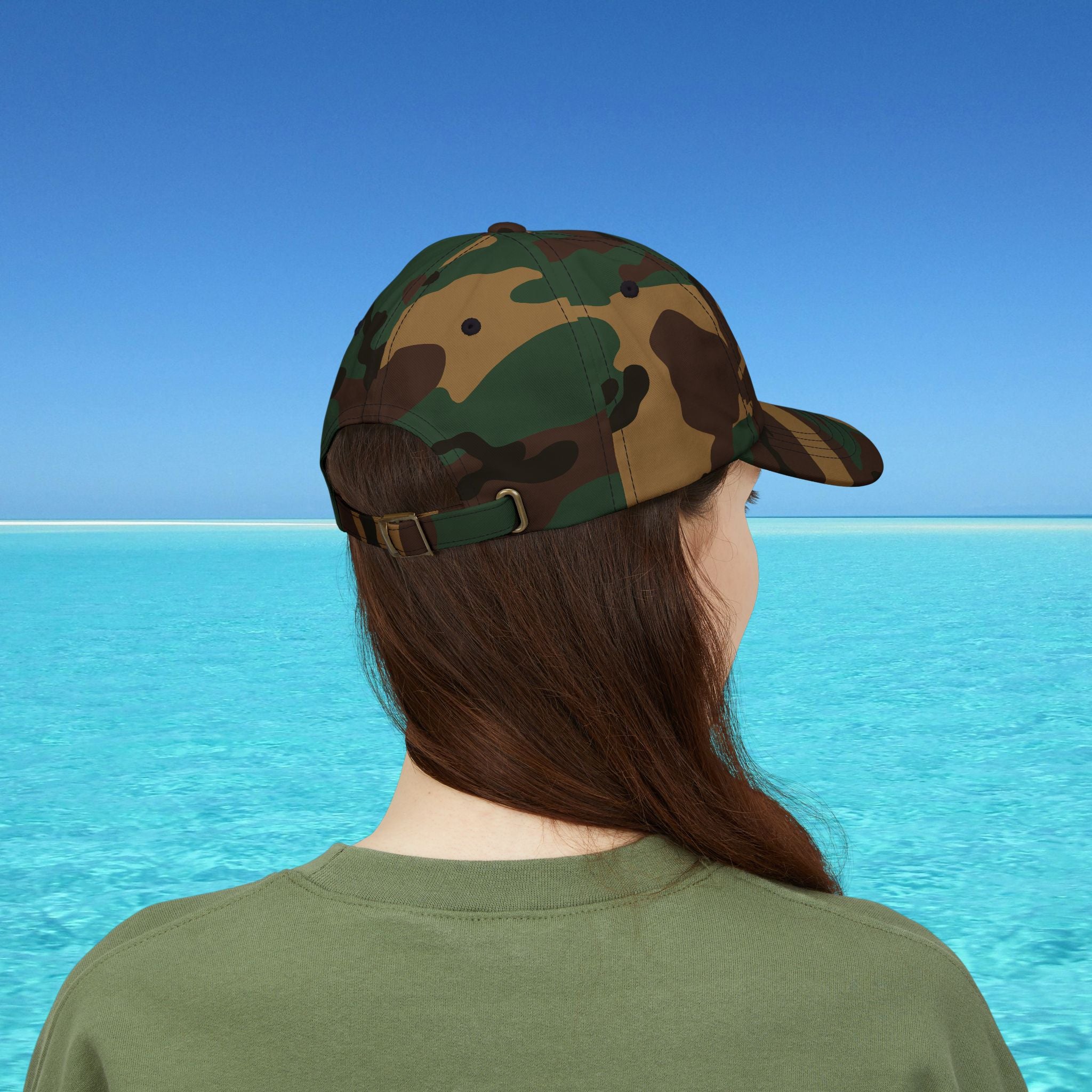 Person wearing a camouflage cap and green shirt looking at a blue ocean