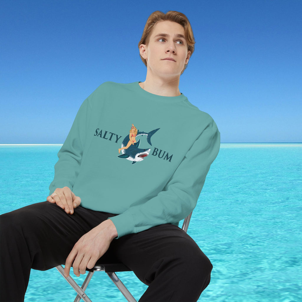 Person wearing a teal sweatshirt with a graphic design sitting on a beach.