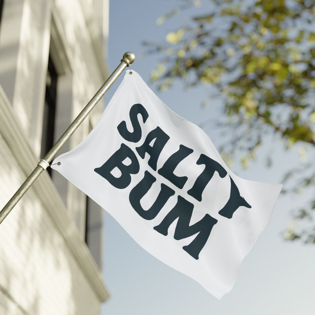 Flag with 'Salty Bum' text waving in front of a building and tree.