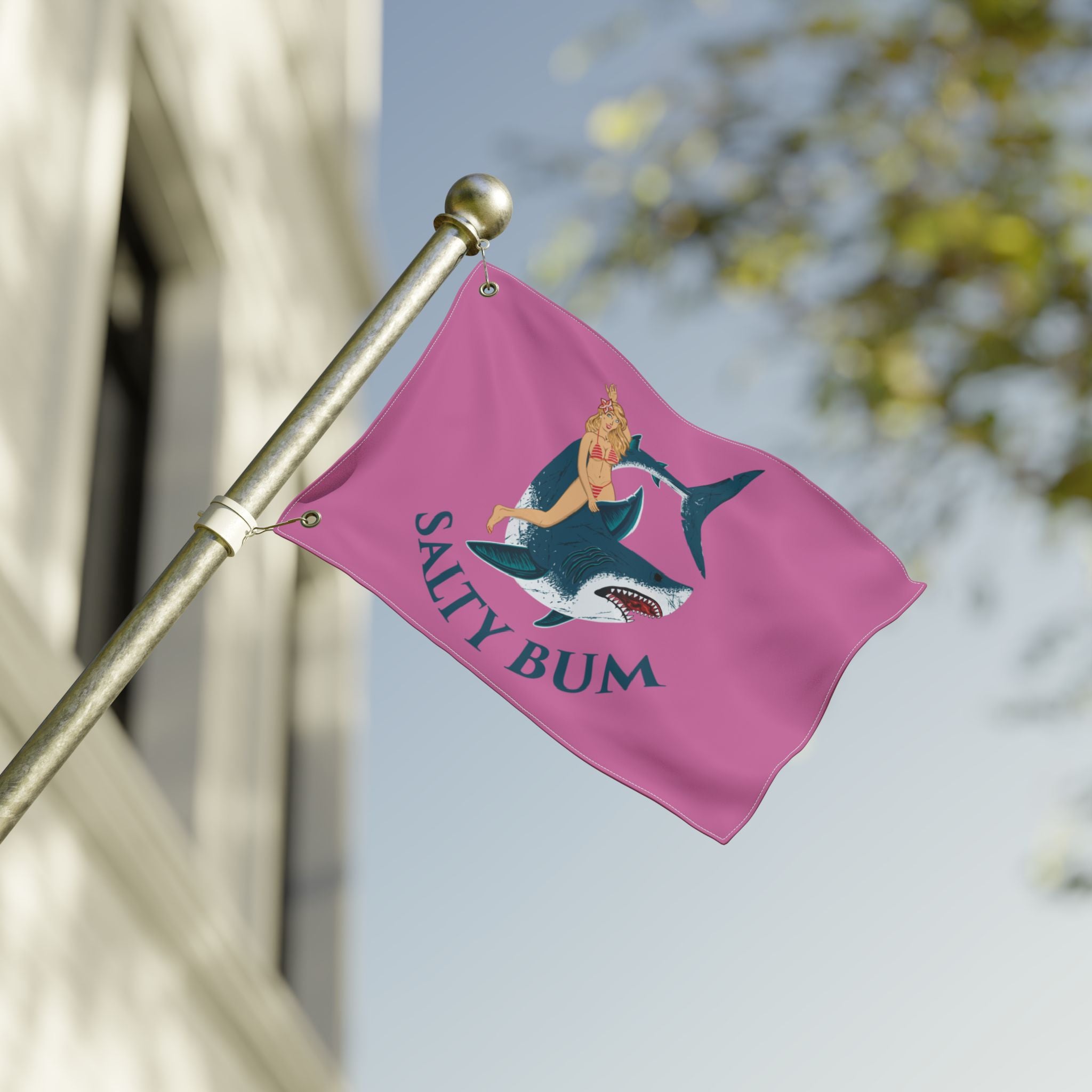 Pink flag with a graphic design of a woman on a shark and 'Salty Bum' text, attached to a pole outdoors.