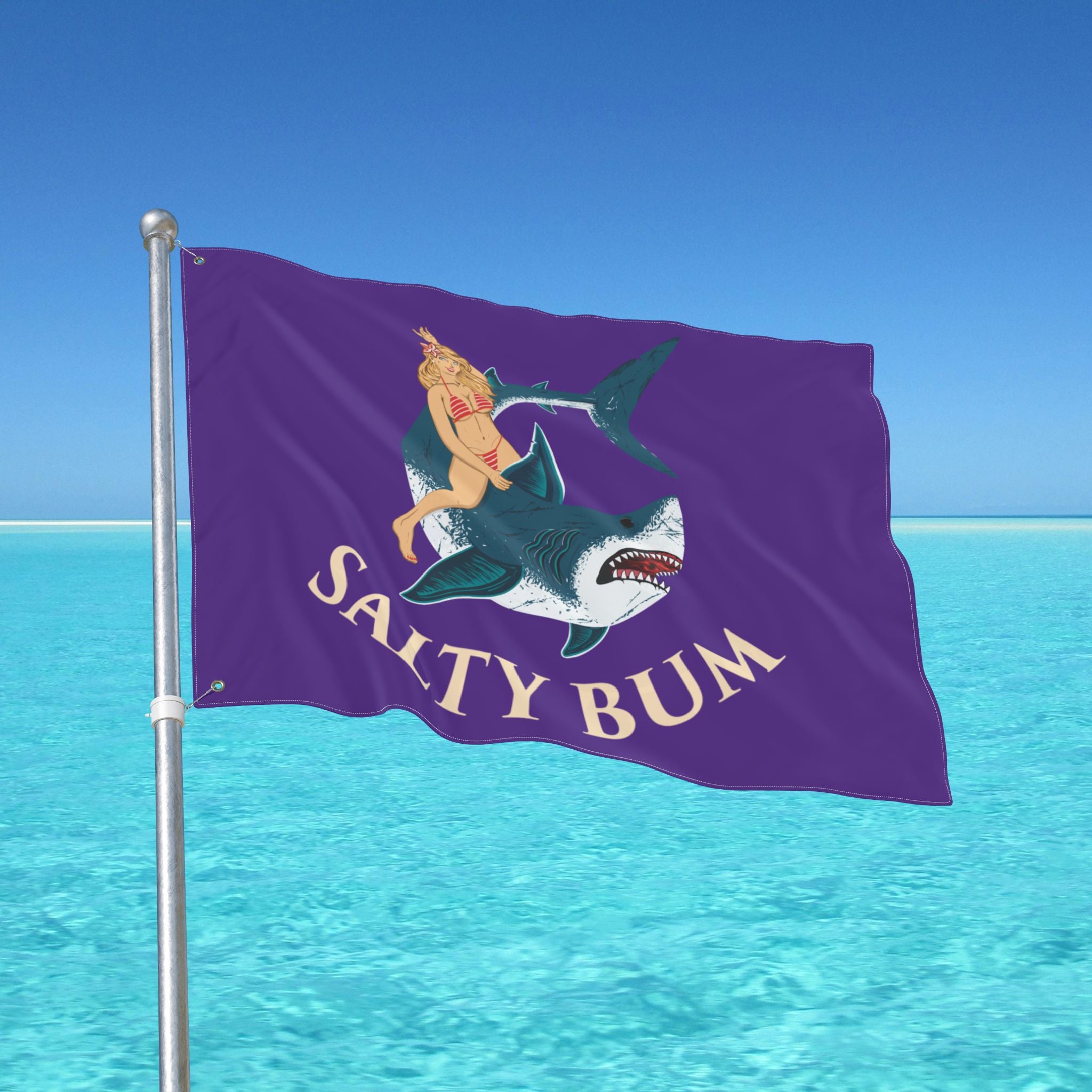 Flag with a shark and mermaid design on a pole against a clear blue sky.