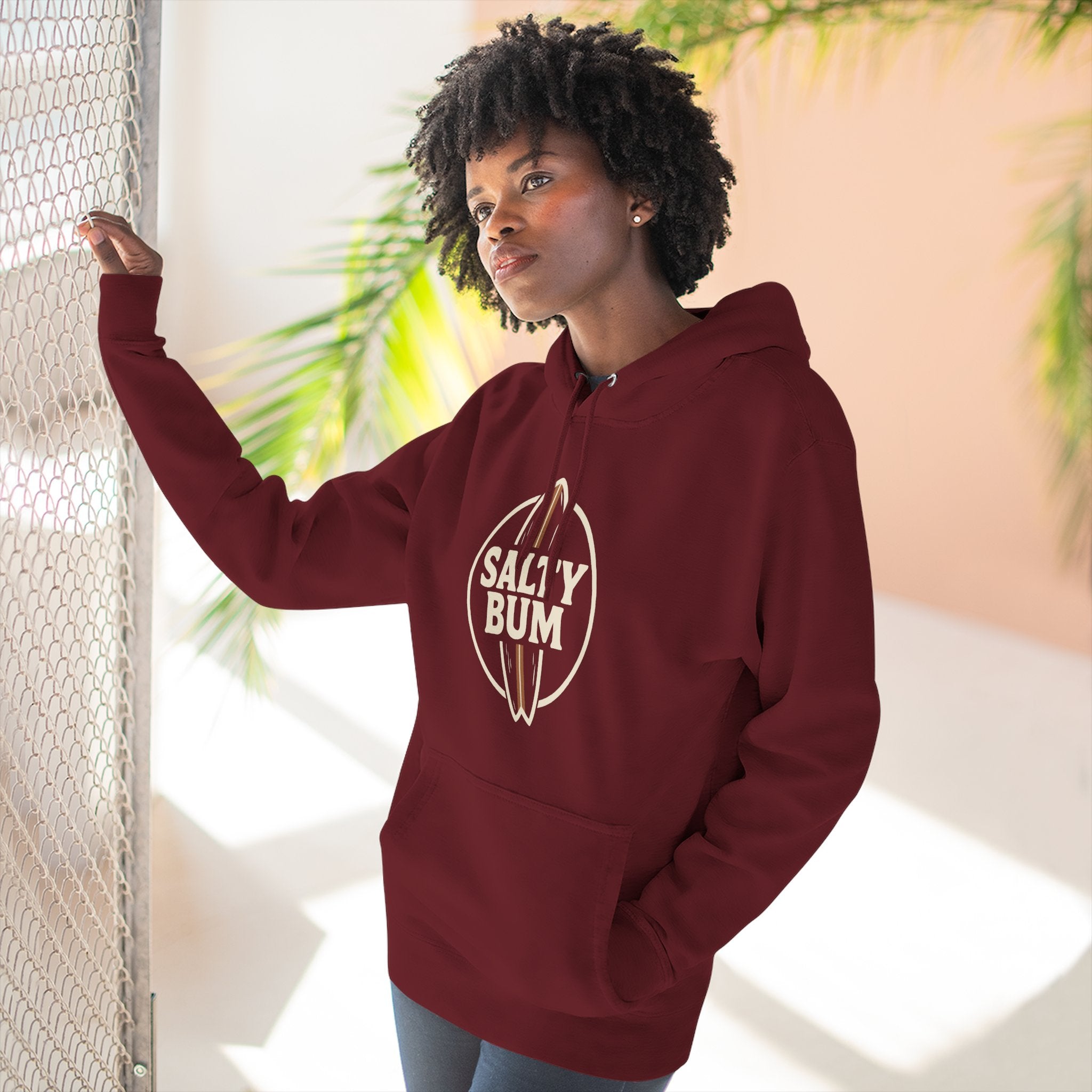 Woman wearing a maroon hoodie with 'Salty Bum' logo, standing indoors with plants in the background