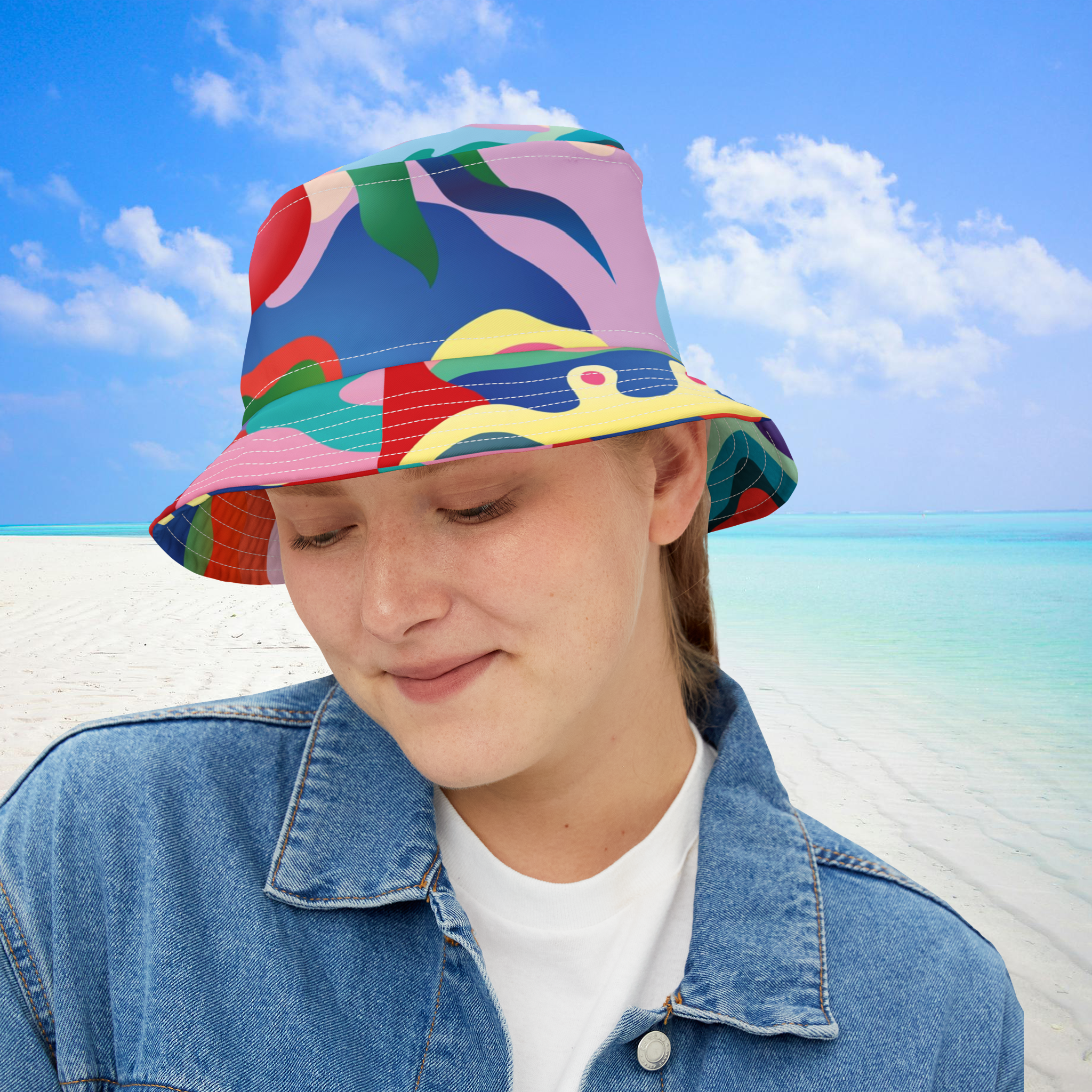 Person wearing a colorful bucket hat on a beach with blue sky and ocean.