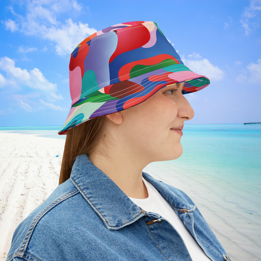 Person wearing a colorful bucket hat on a beach with blue sky and ocean.