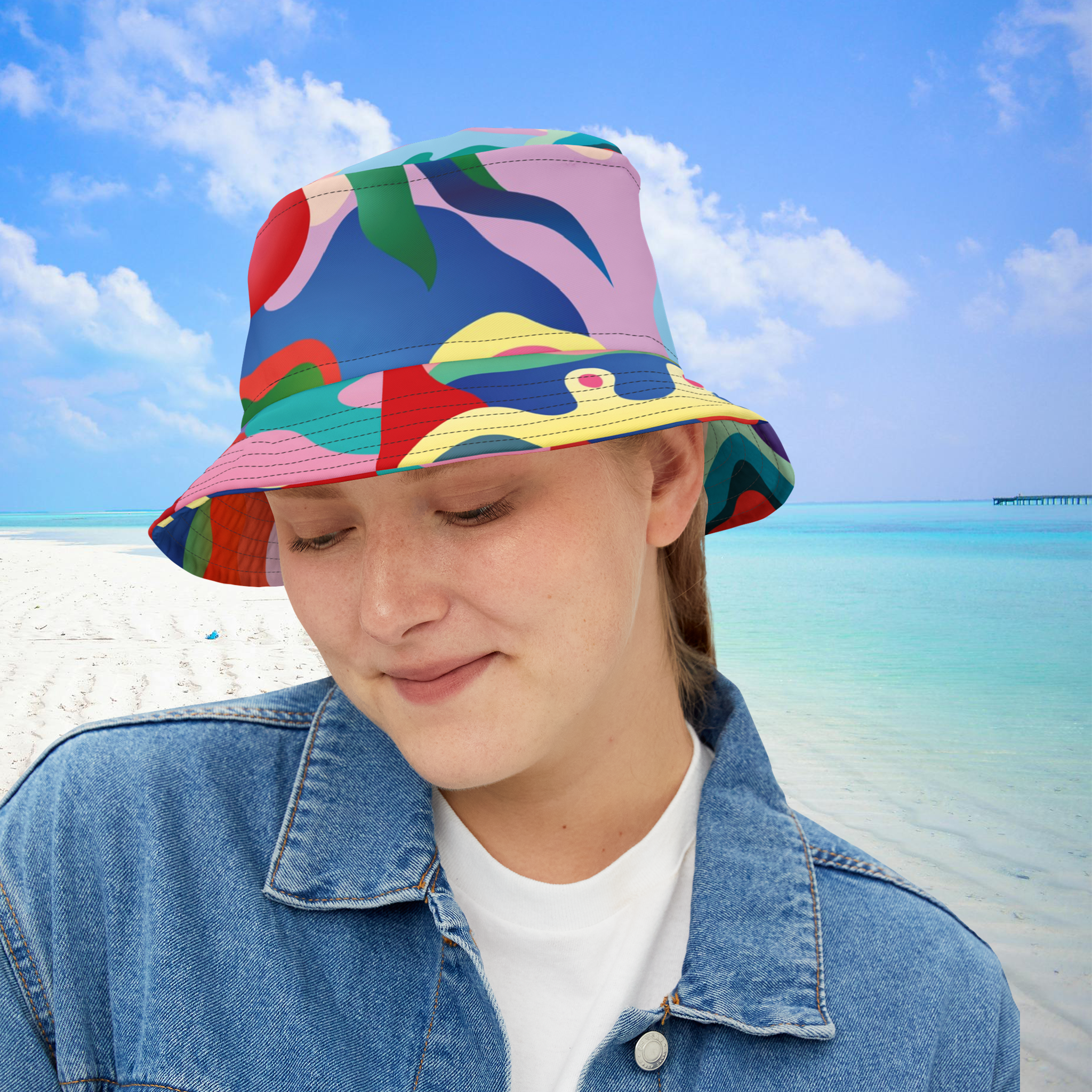 Person wearing a colorful bucket hat on a beach with blue sky and ocean.