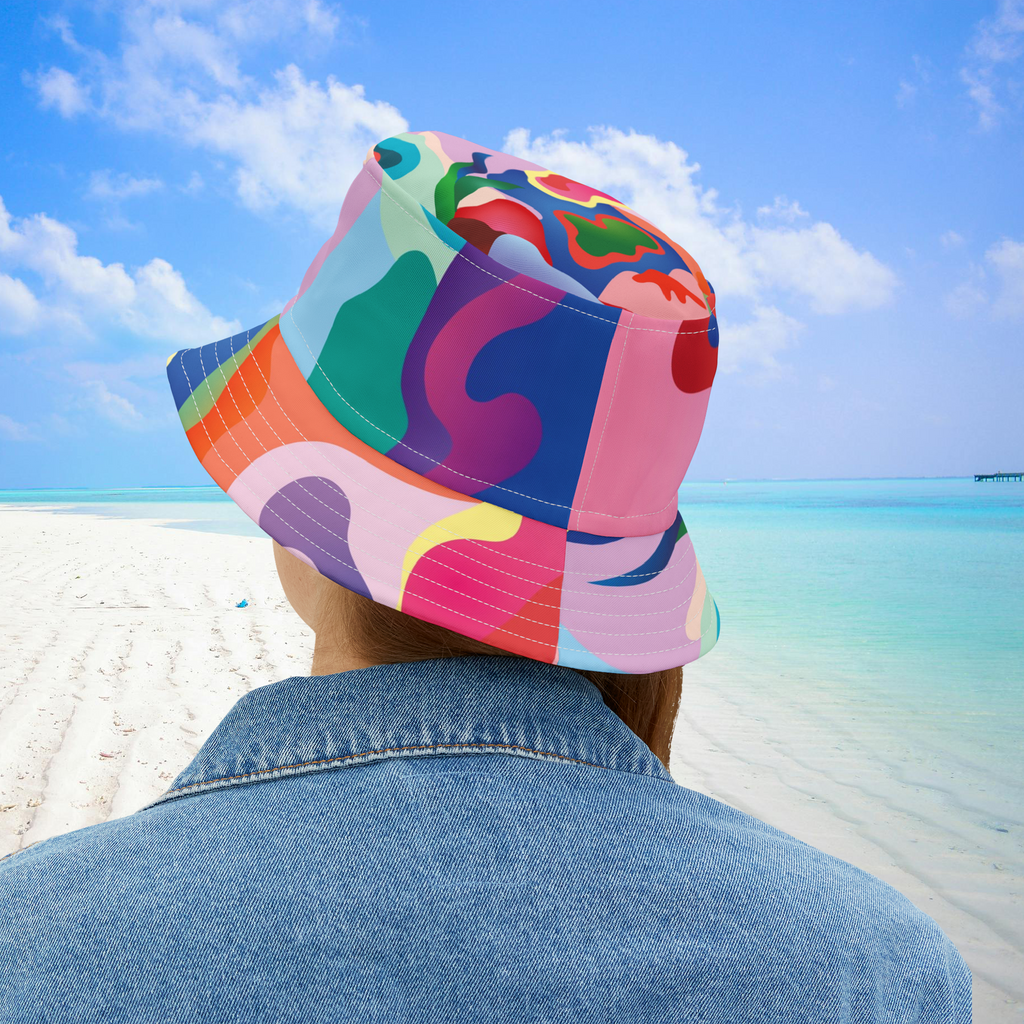 Person wearing a colorful bucket hat on a beach with blue sky and ocean.