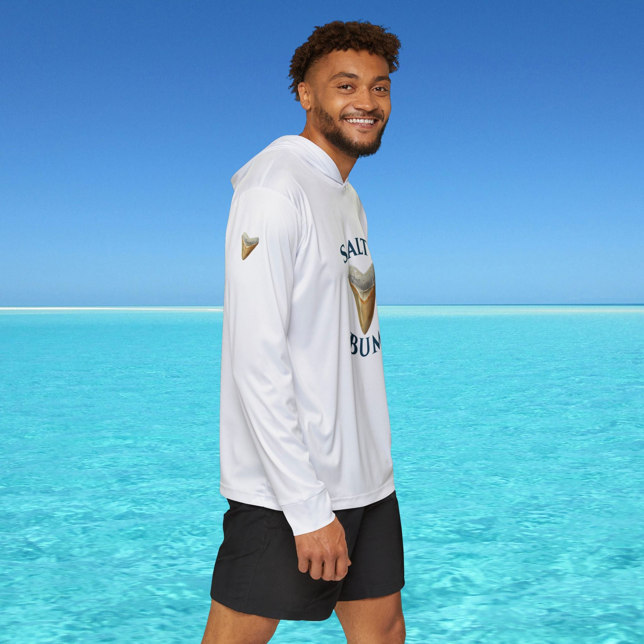 Man wearing a white hoodie with branding standing in front of clear blue water and sky.