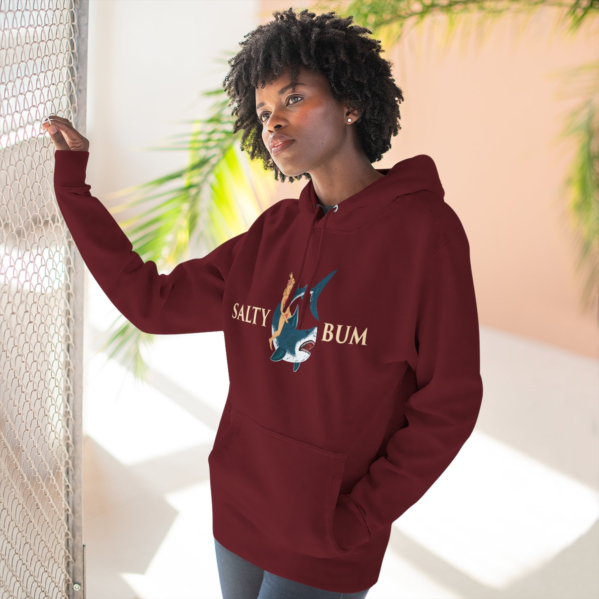 Person wearing a maroon hoodie with 'Salty Bum' logo, standing indoors with plants in the background