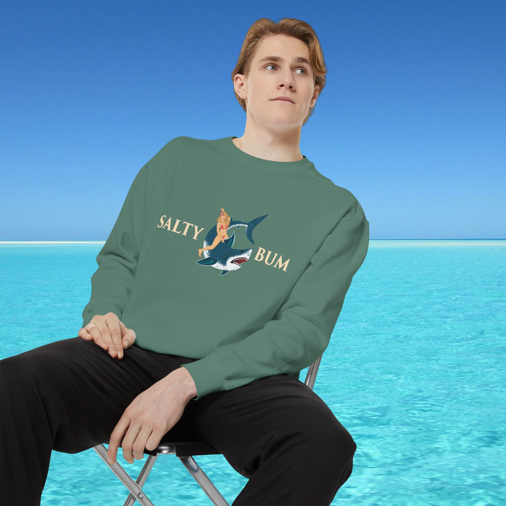 Person wearing a green sweatshirt with a graphic design sitting on a chair in front of a blue water background.