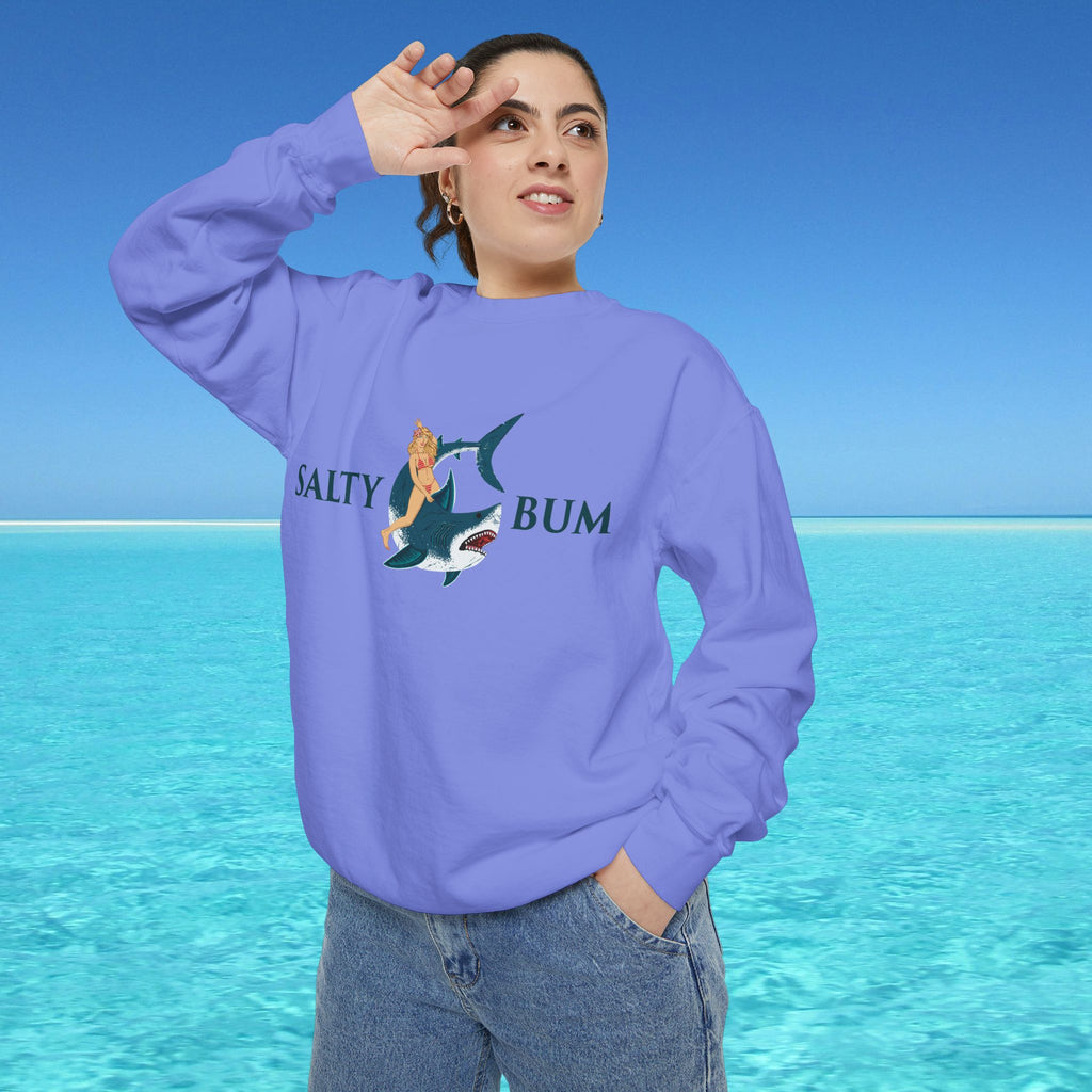 Person wearing a purple sweatshirt with a graphic design and text, standing against a blue sky and water background.