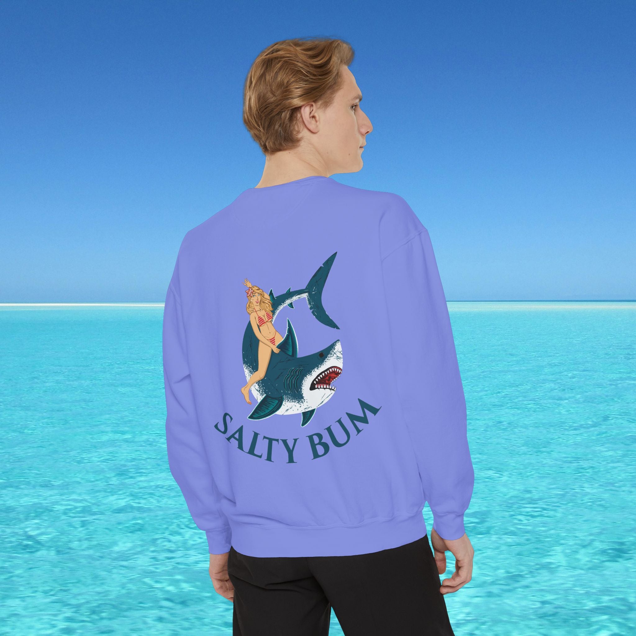 Person wearing a purple sweatshirt with a shark and bikini graphic and 'Salty Bum' text, standing in front of a blue ocean.