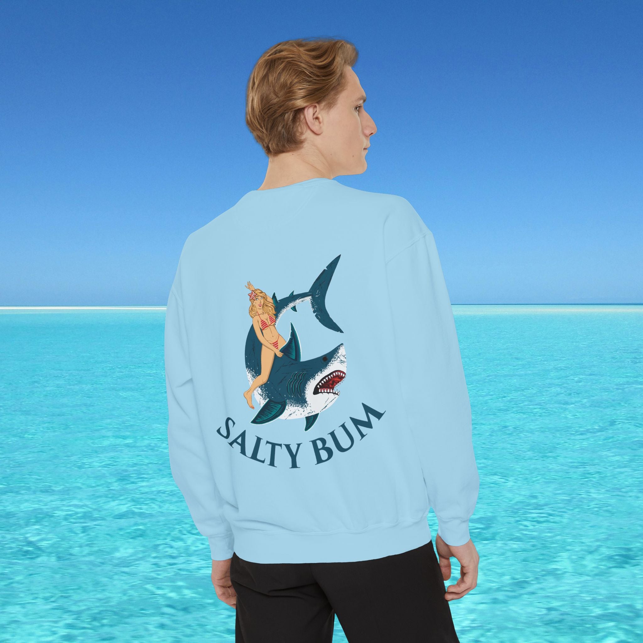 Person wearing a light blue sweatshirt with a shark and bikini graphic and 'Salty Bum' text, standing in front of a blue ocean.