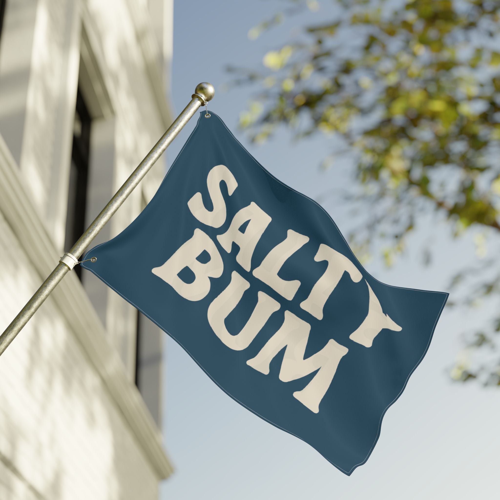 Flag with 'Salty Bum' text waving in front of a building and tree.