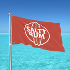 Red flag with 'Salty Rum' logo against a clear blue sky and ocean.