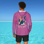 Person wearing a pink hoodie with a shark graphic and 'Salty Bun' text, standing in front of clear blue water.