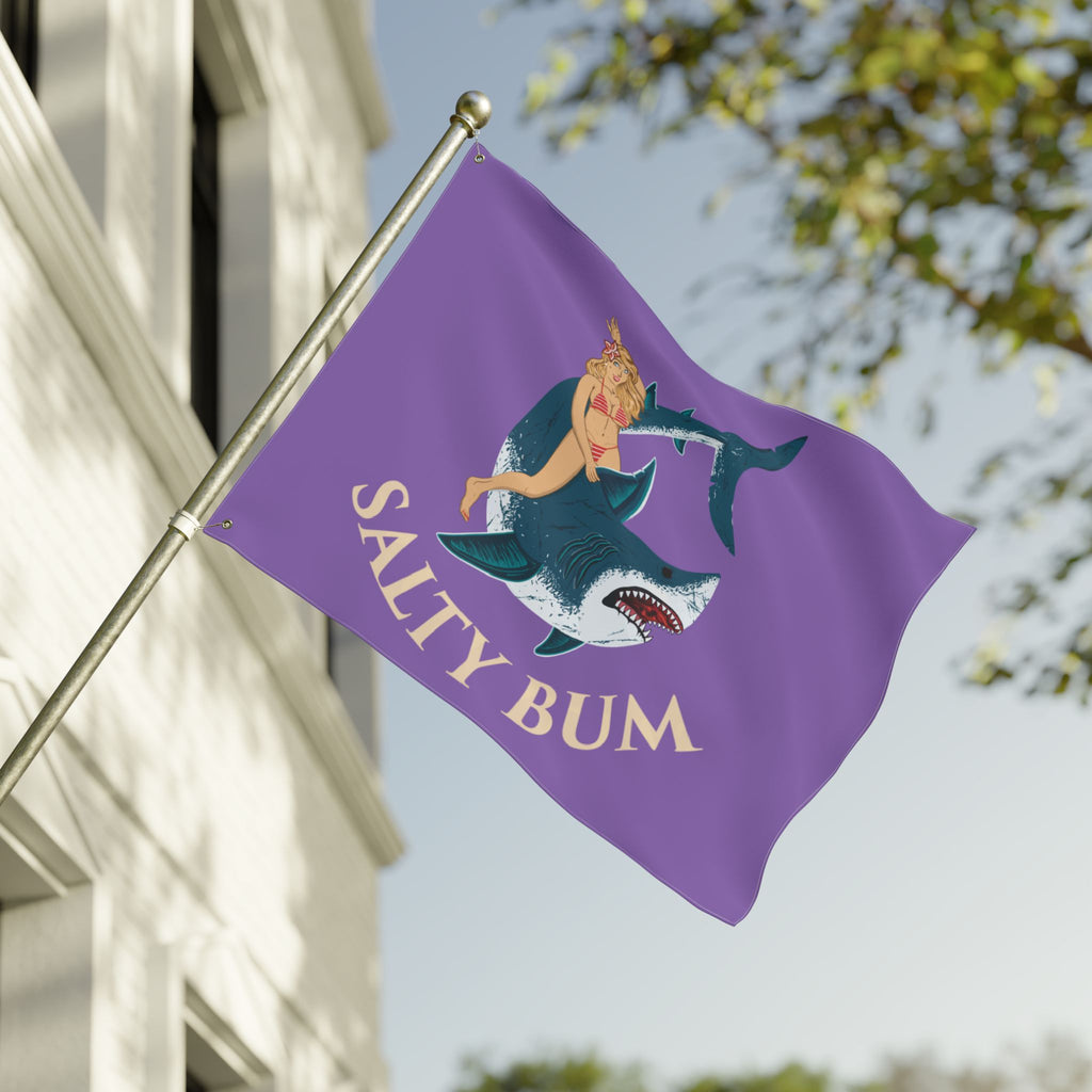 Purple flag with a mermaid and shark design and 'Salty Bum' text, waving in front of a building.