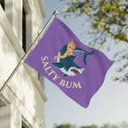 Purple flag with a mermaid and shark design and 'Salty Bum' text, waving in front of a building.