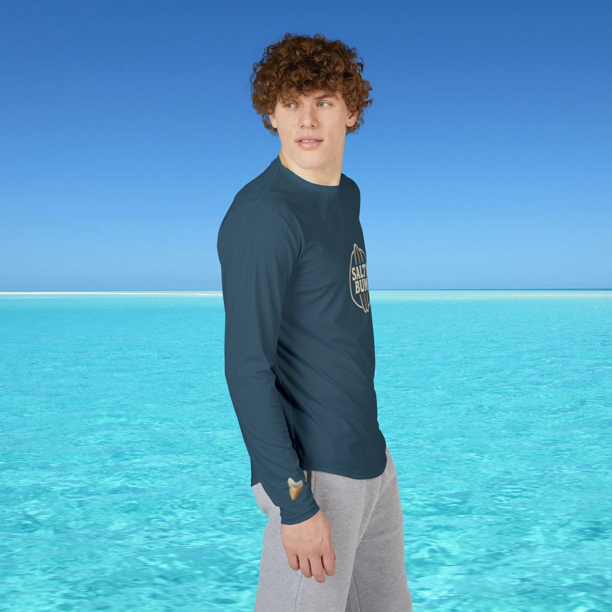 Person wearing a blue long-sleeve shirt with a logo standing in front of clear blue water and sky.