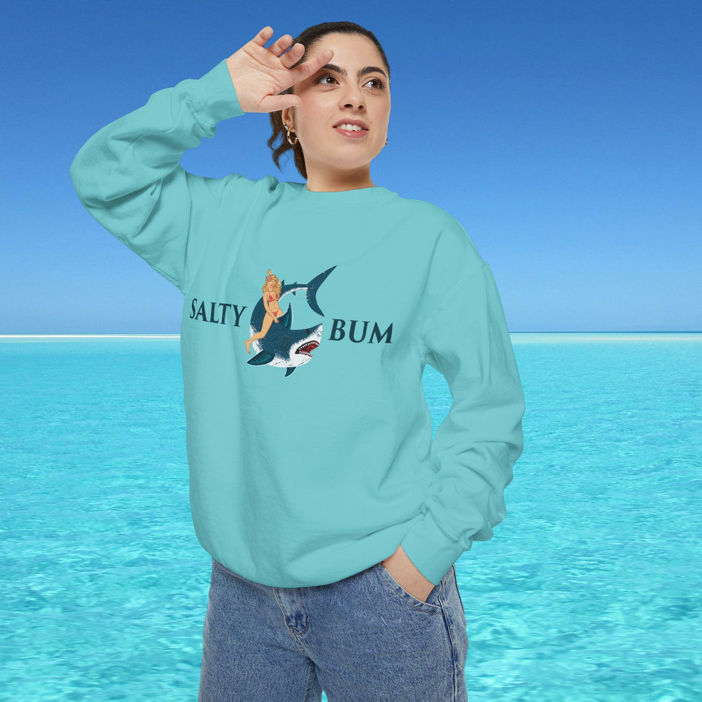 Person wearing a light blue sweatshirt with a graphic design and text, standing against a clear blue sky and ocean.