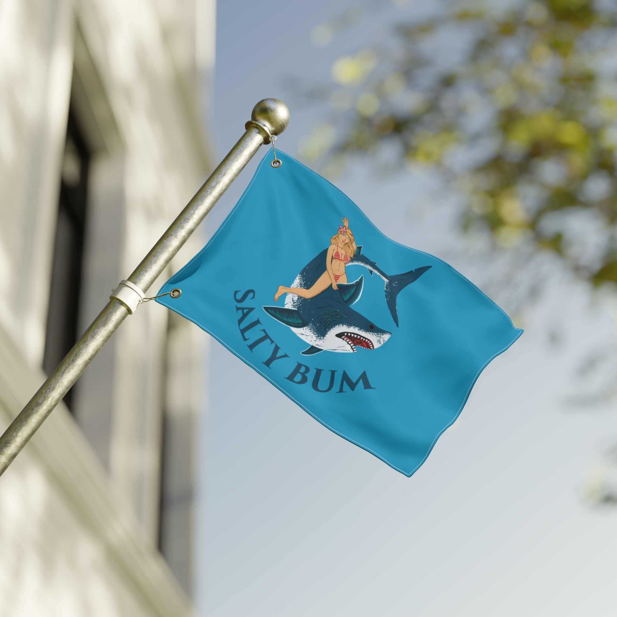 Teal flag with a shark and bikini-clad figure design, featuring the text 'Salty Bum', on a pole against a blurred background.