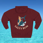 Maroon hoodie with a graphic of a woman on a shark and 'Salty Bum' text, set against a blue water and sky background.
