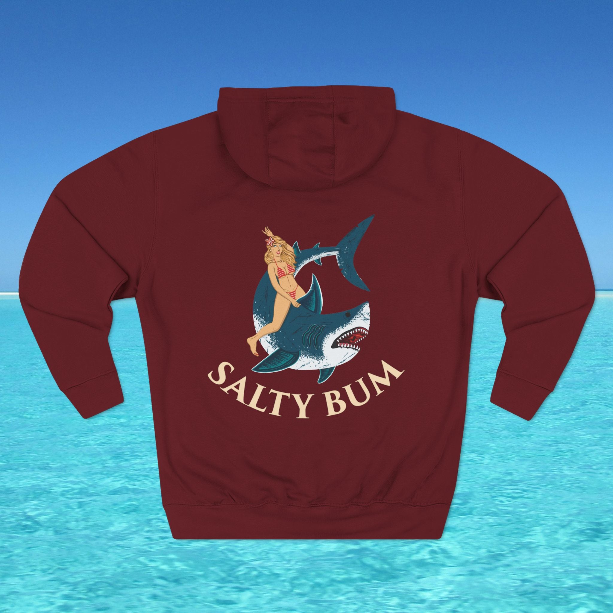 Maroon hoodie with a graphic of a woman on a shark and 'Salty Bum' text, set against a blue water and sky background.