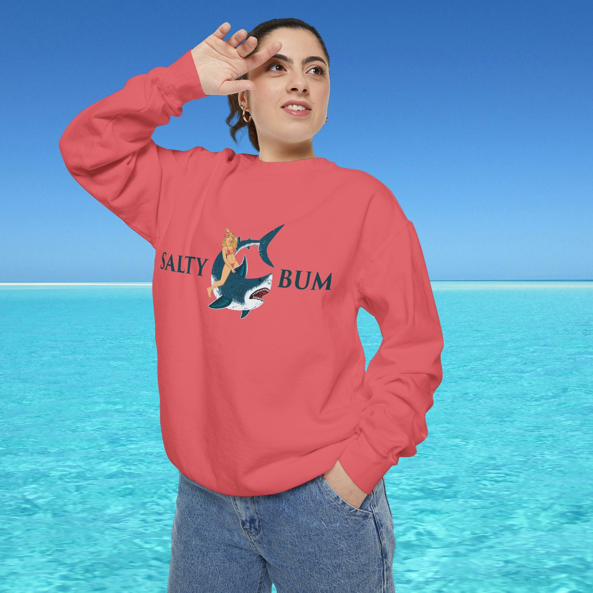 Person wearing a red sweatshirt with a shark graphic and text, standing in front of a blue ocean.