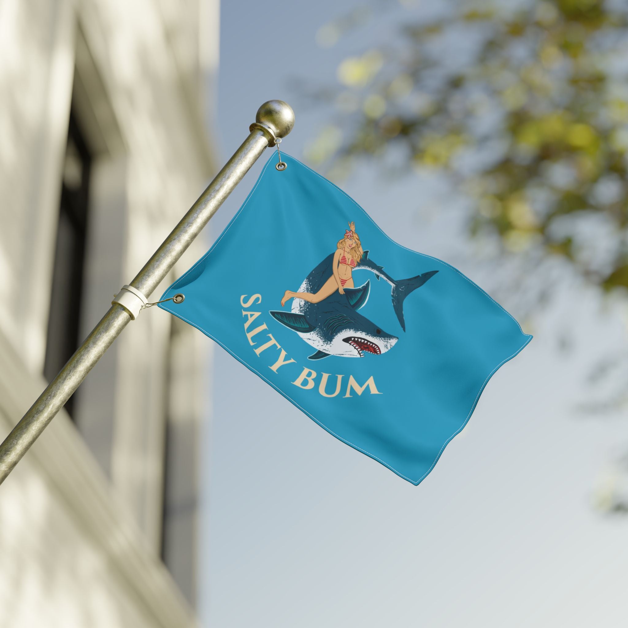 Flag with a shark and woman design and 'Salty Bum' text on a pole against a blurred background