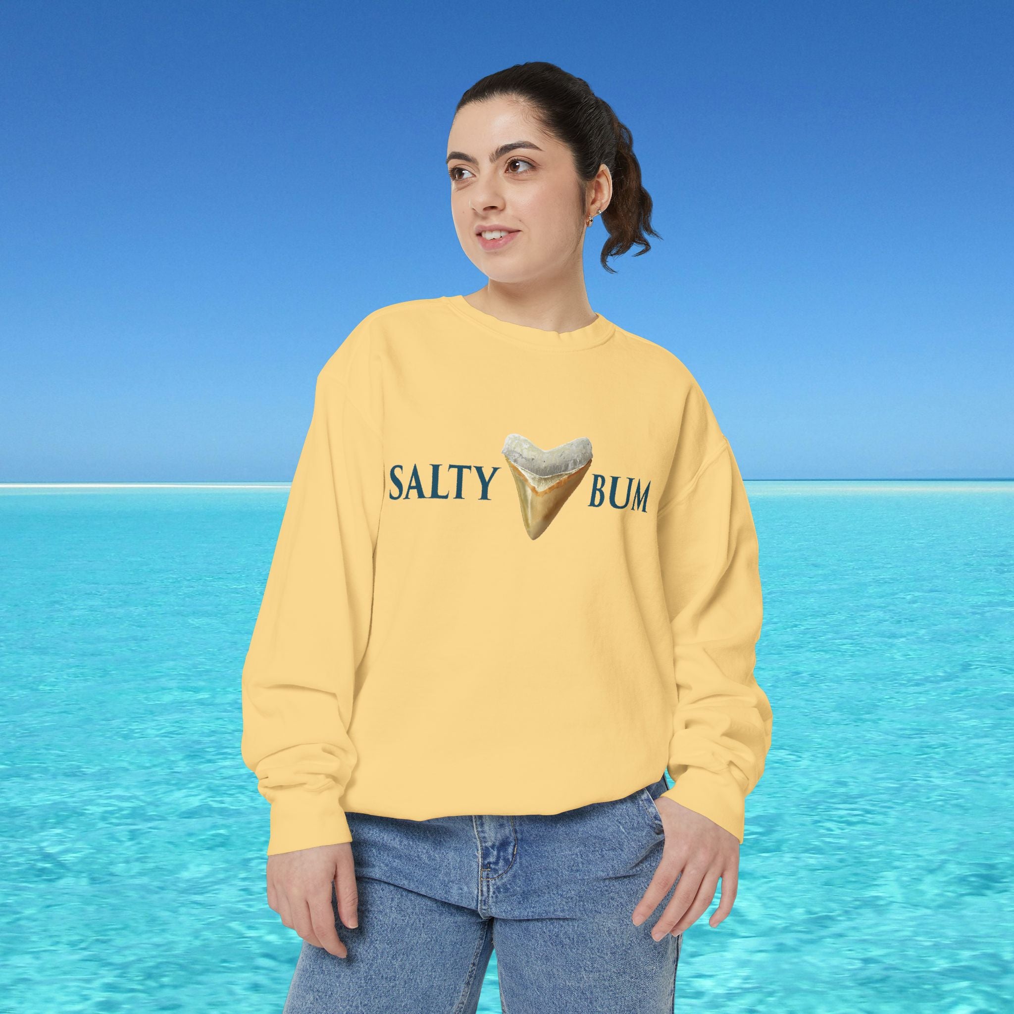 Person wearing a yellow sweatshirt with 'Salty Bum' text and ice cream graphic against a blue ocean background