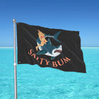 Flag with a shark and bikini-clad figure design against a blue ocean background