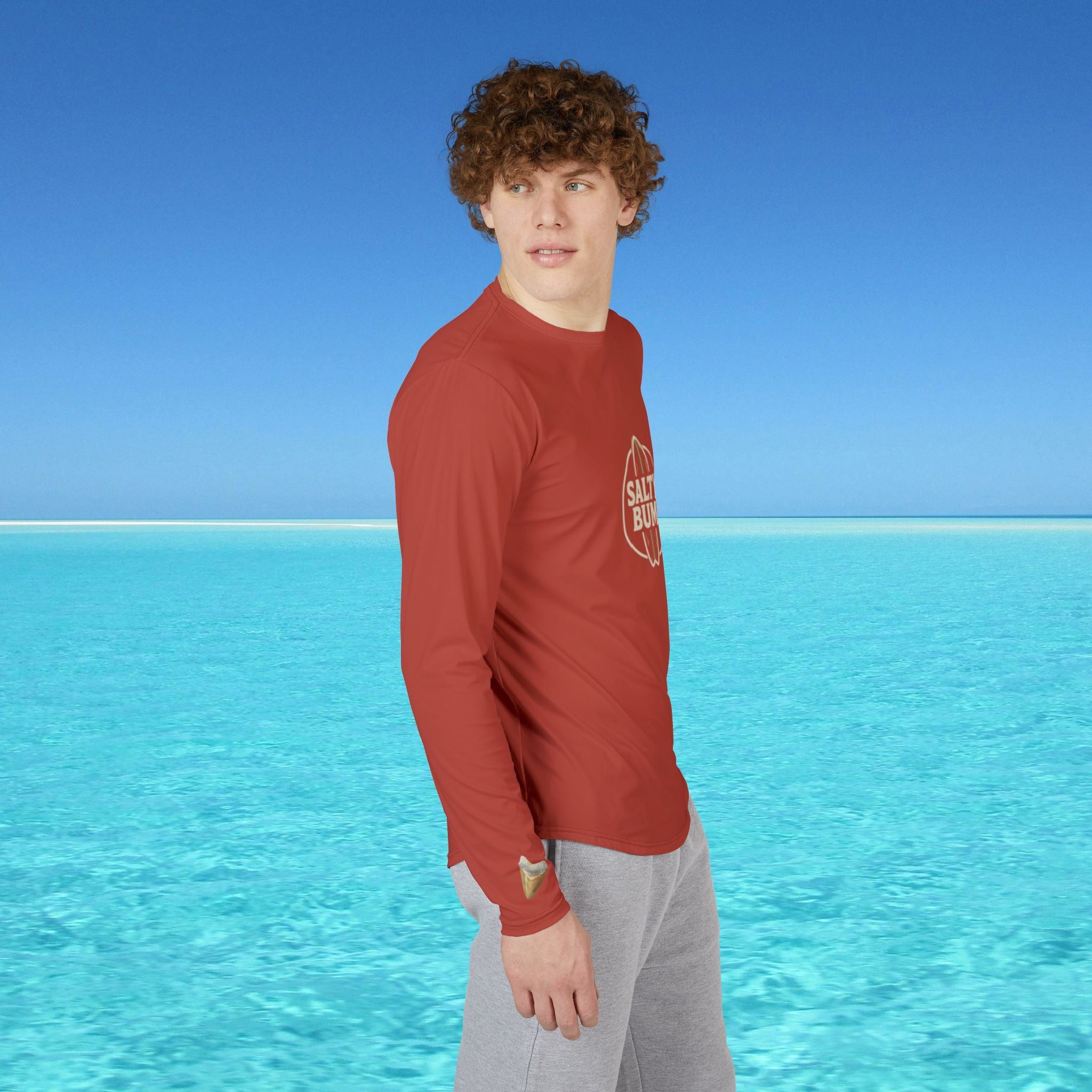 Person wearing a red shirt with a logo standing in front of clear blue water and sky.