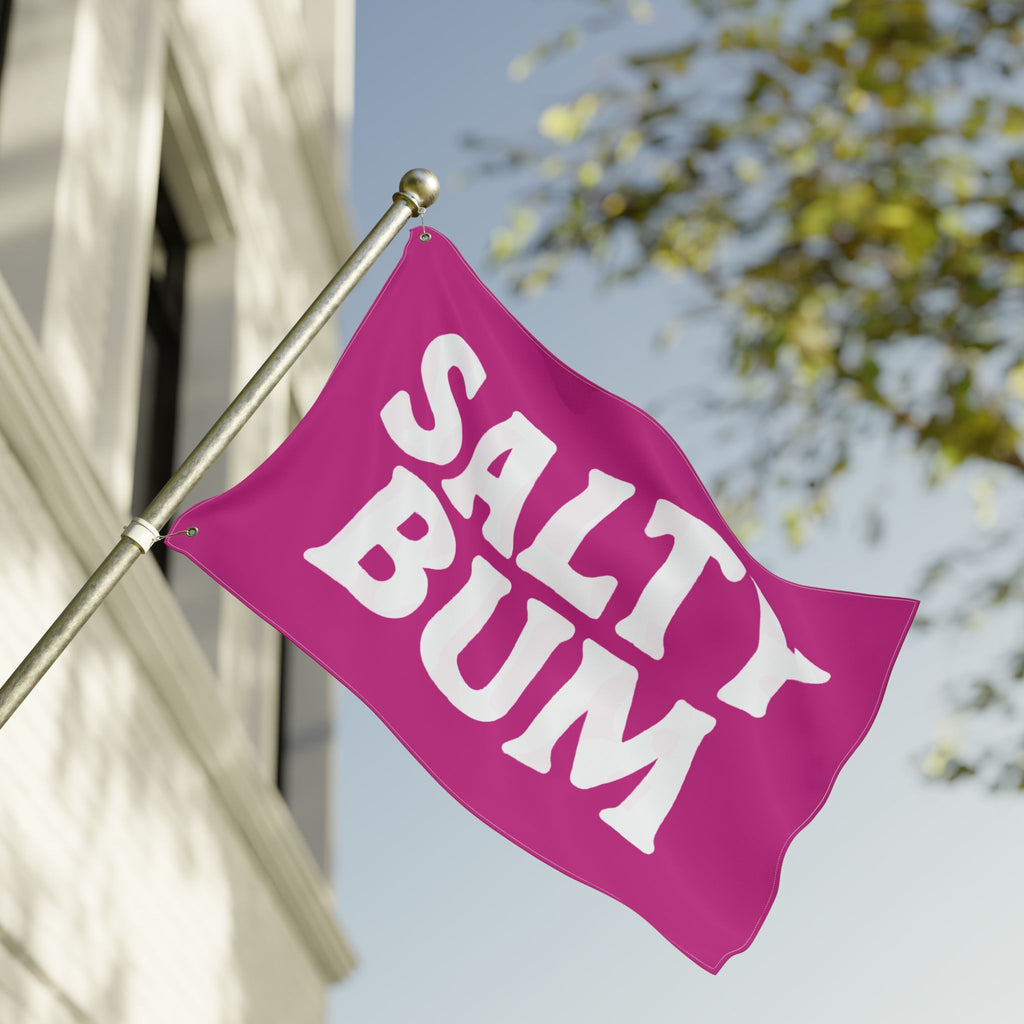 Pink flag with 'Salty Bum' text waving in front of a building and tree.
