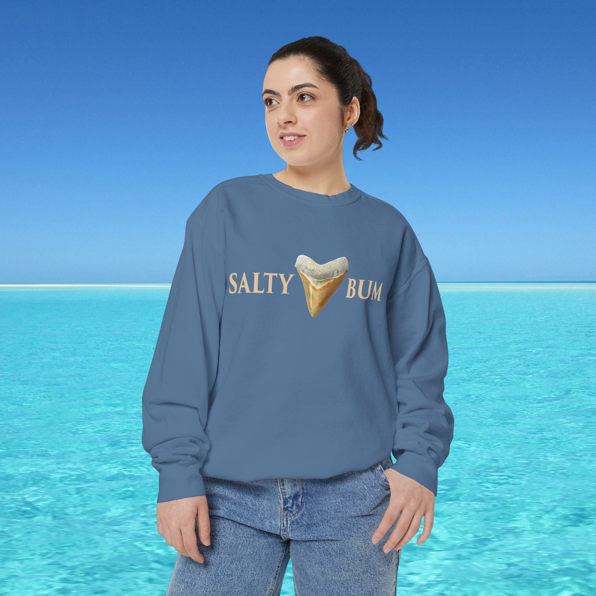Person wearing a blue sweatshirt with 'Salty Bum' text and ice cream graphic against a blue sky and ocean background.
