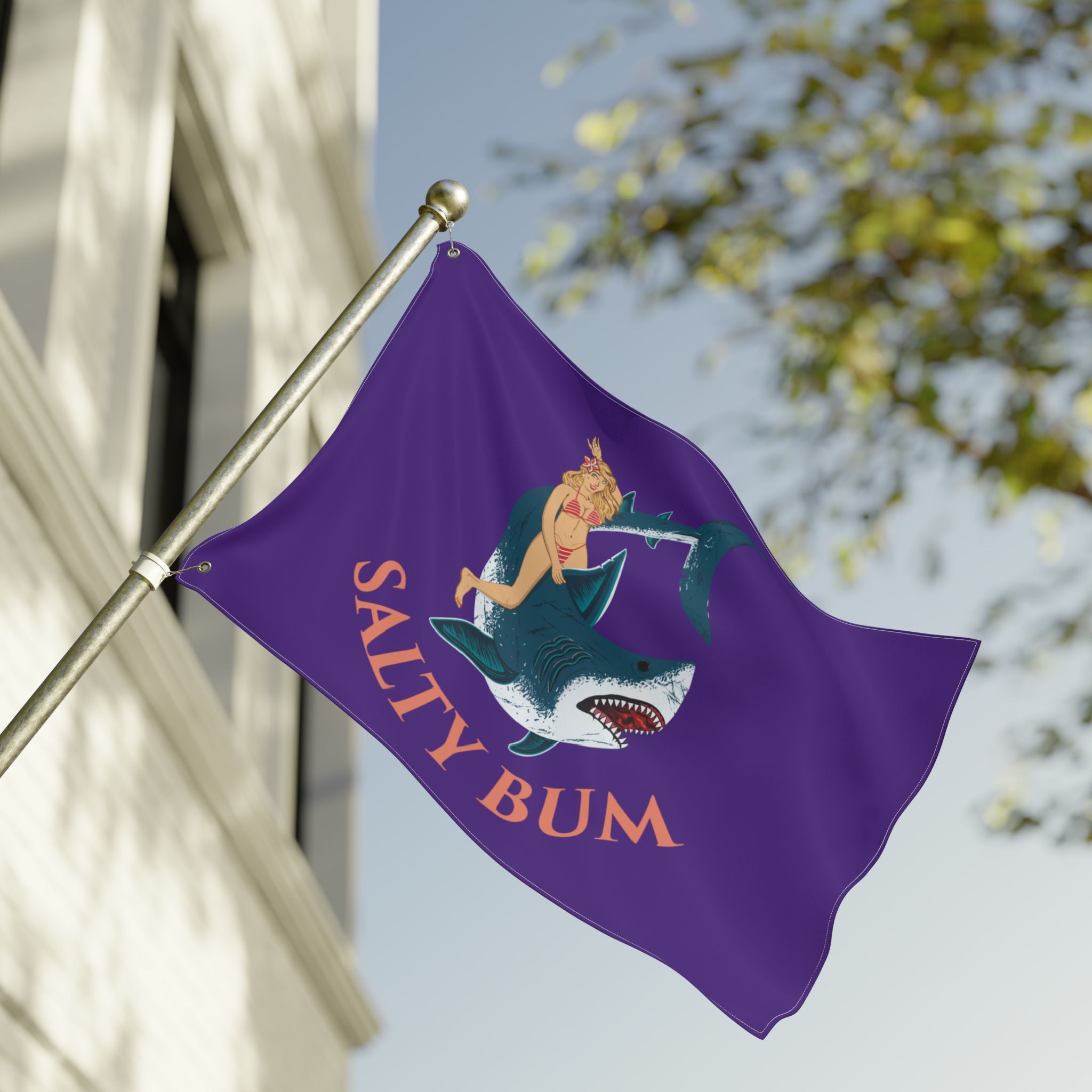 Purple flag with a shark and mermaid design and 'Salty Bum' text, waving in front of a building.