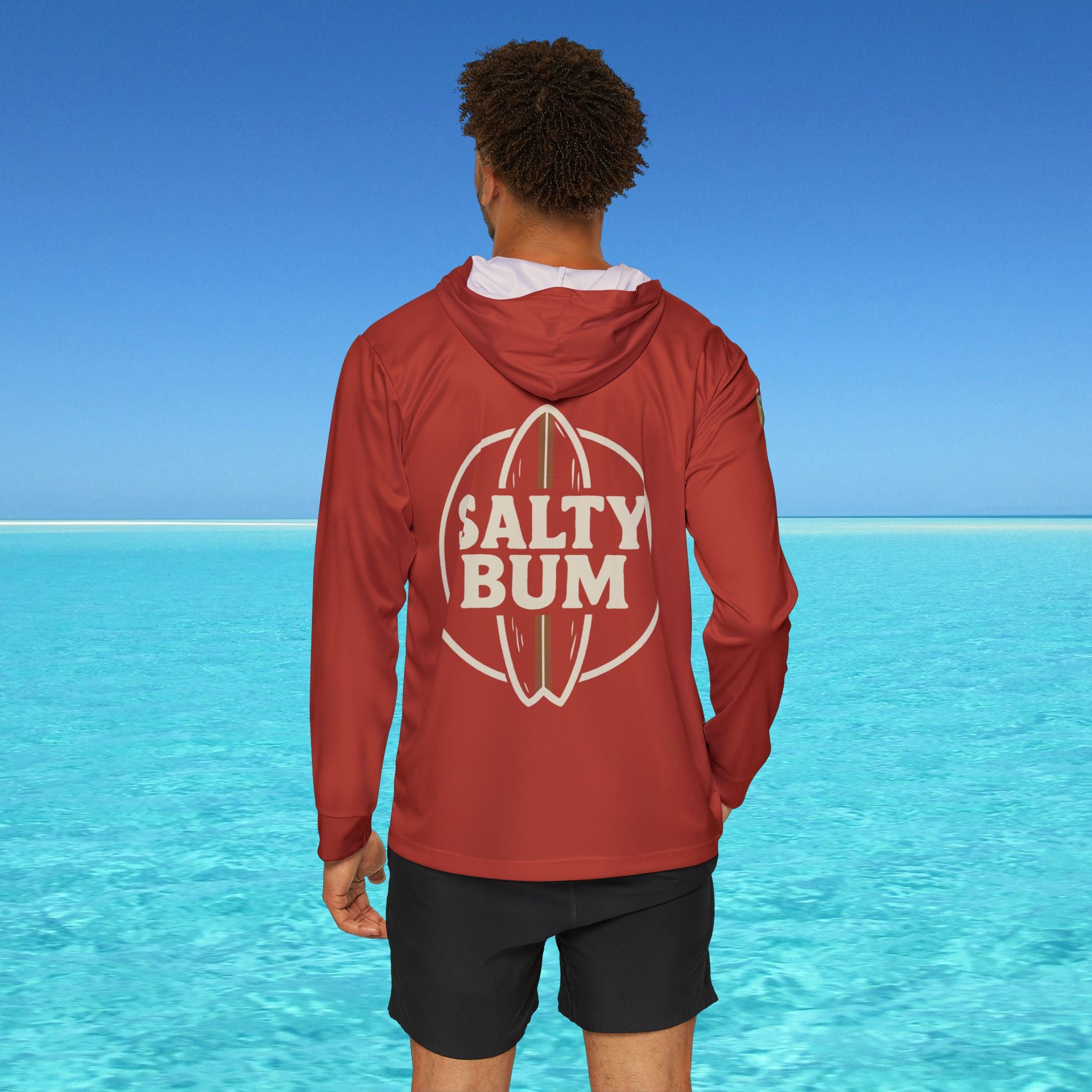 Person wearing a red hoodie with 'Salty Bum' logo by a clear blue ocean.