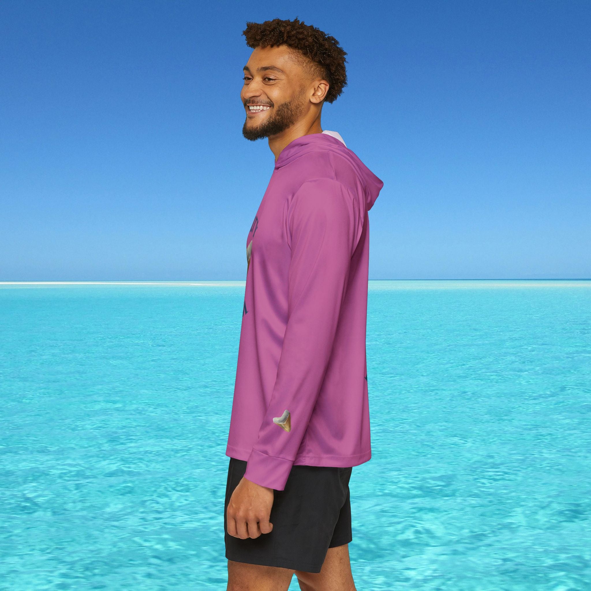Man wearing a purple jacket standing on a beach with clear blue water and sky.