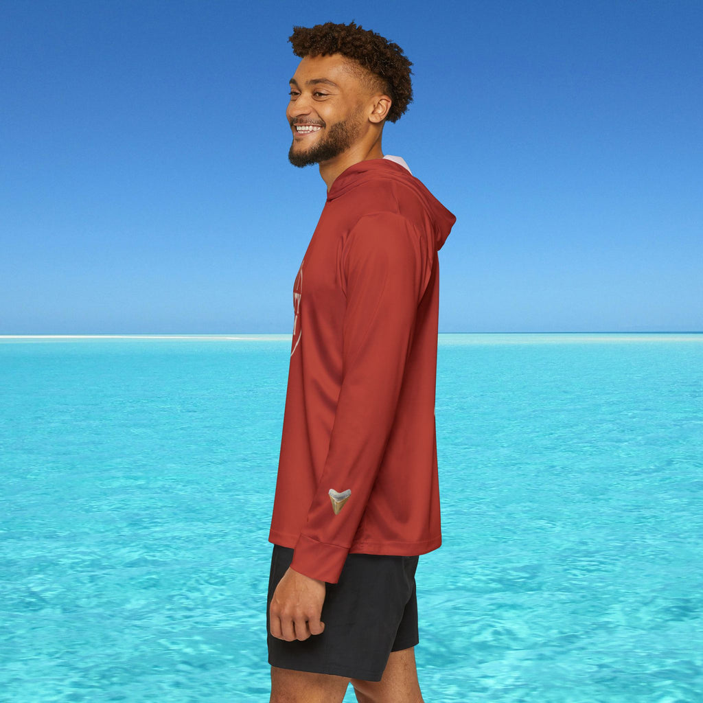 Man wearing a red jacket standing on a beach with clear blue water and sky.