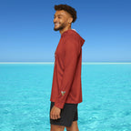 Man wearing a red jacket standing on a beach with clear blue water and sky.