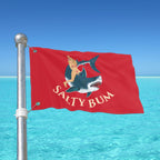 Red flag with 'Salty Bum' design featuring a mermaid and shark against a clear blue sky.