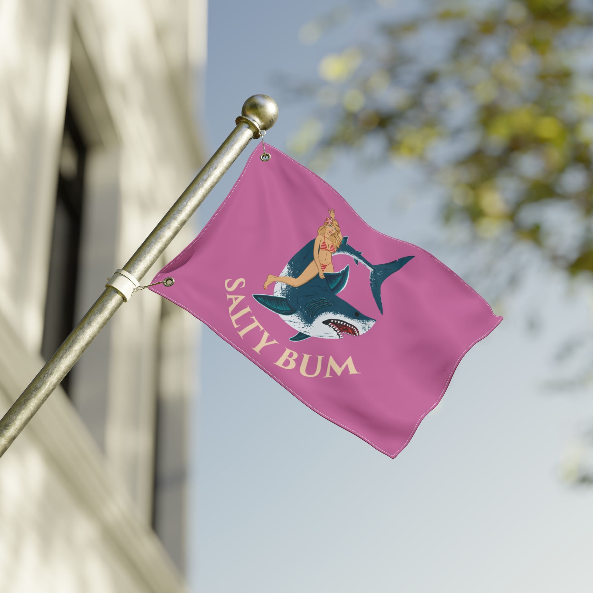 Pink flag with a graphic of a woman on a shark and 'Salty Bum' text, attached to a pole outdoors.