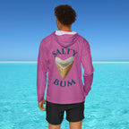Person wearing a pink hoodie with 'Salty Bum' text and ice cream graphic in front of a clear blue ocean.