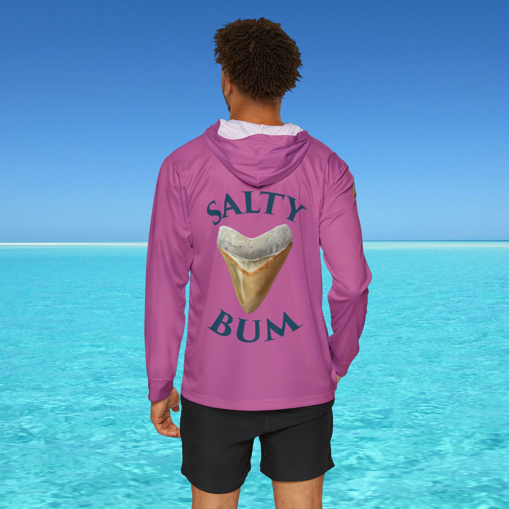Person wearing a pink hoodie with 'Salty Bum' text and ice cream graphic in front of a clear blue ocean.